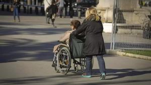 Una persona en silla de ruedas, acompañada de una cuidadora, en Barcelona.