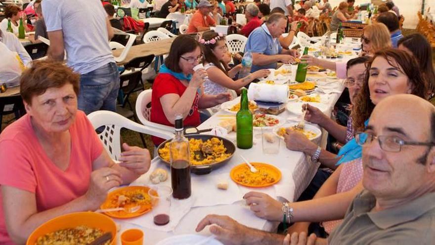 Un grupo de vecinos degusta la paella bajo la carpa de la fiesta.