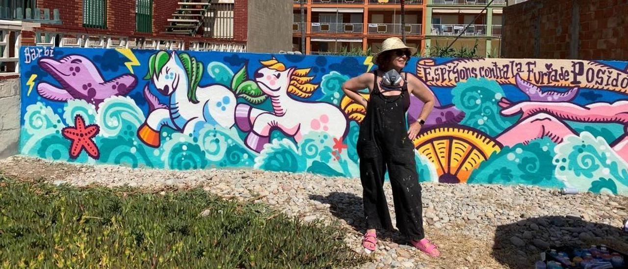 La artista urbana Barbiturikills posa junto a uno de los dos murales que ha creado en los accesos a la playa de Nules.