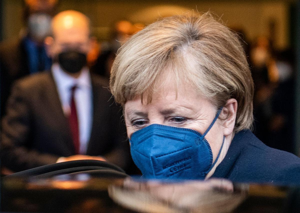 Olaf Scholz, en segundo plano, observa como Angela Merkel abandona el edificio de la cancillería y sube a un automóvil.