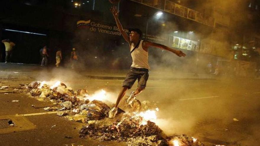 Un joven opositor salta sobre los restos de una barricada de basura incendiada en Caracas.  // Reuters
