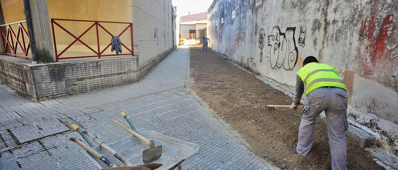 Dos operarios municipales preparan una zona de patio en el colegio de A Escardia.