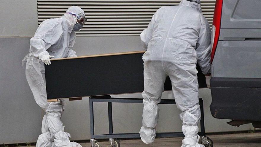 Dos operarios con trajes de protección y mascarillas trasladan el cuerpo de un fallecido con coronavirus.
