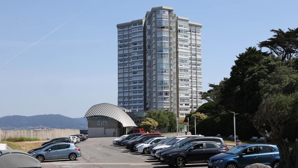 Coches aparcados en la isla de Toralla, con la torre de viviendas al fondo.