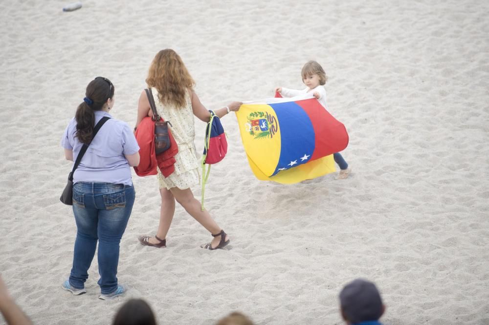 La comunidad venezolana despliega en la playa de Riazor una bandera para exigir que su país sea "libre".