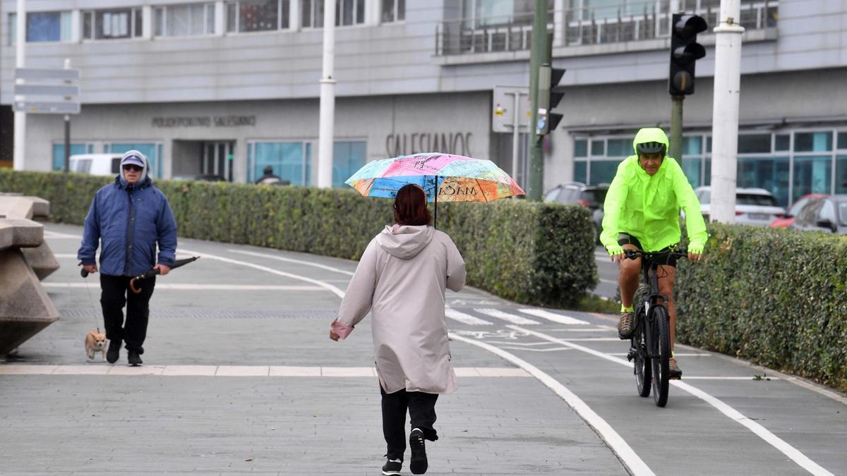 Varias personas en el paseo marítimo de A Coruña un día con algunos chubascos débiles.