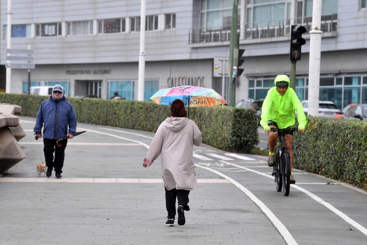 Varias personas en el paseo marítimo de A Coruña un día con algunos chubascos débiles.
