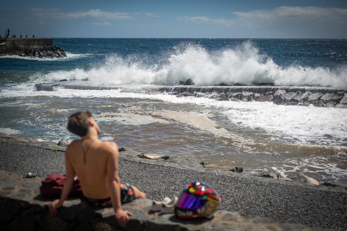 Un joven  toma el sol delante del mar, durante la alerta por fenómenos costeros por Therese.