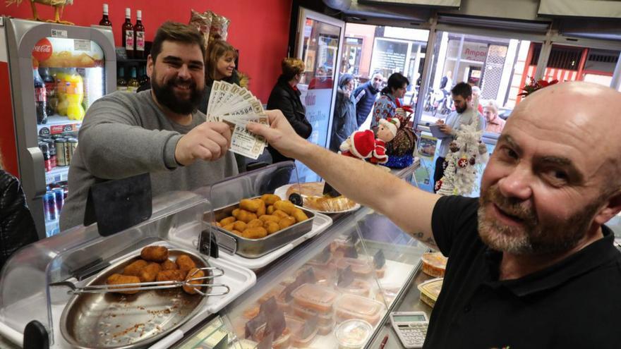 Conrado Álvarez coge varios décimos no premiados a Pablo Pezón a cambio de croquetas, ayer, en su establecimiento de Gijón. | Juan Plaza