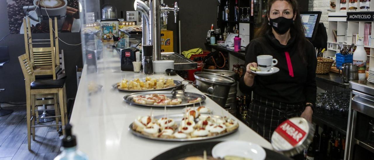 Sandra Alonso se dispone a servir un café para una mesa ante la barra vacía y con las sillas recogidas, en el bar La Tasquita del barrio ovetense de La Corredoria