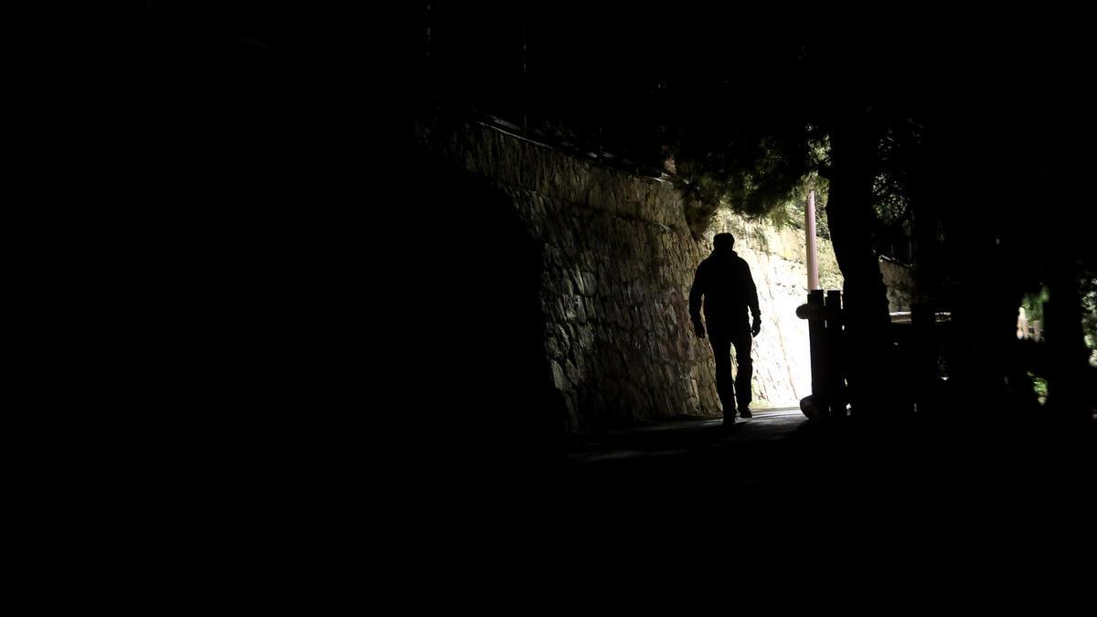 Un joven camina por el sendero que discurre por debajo del colegio La Aneja, a oscuras