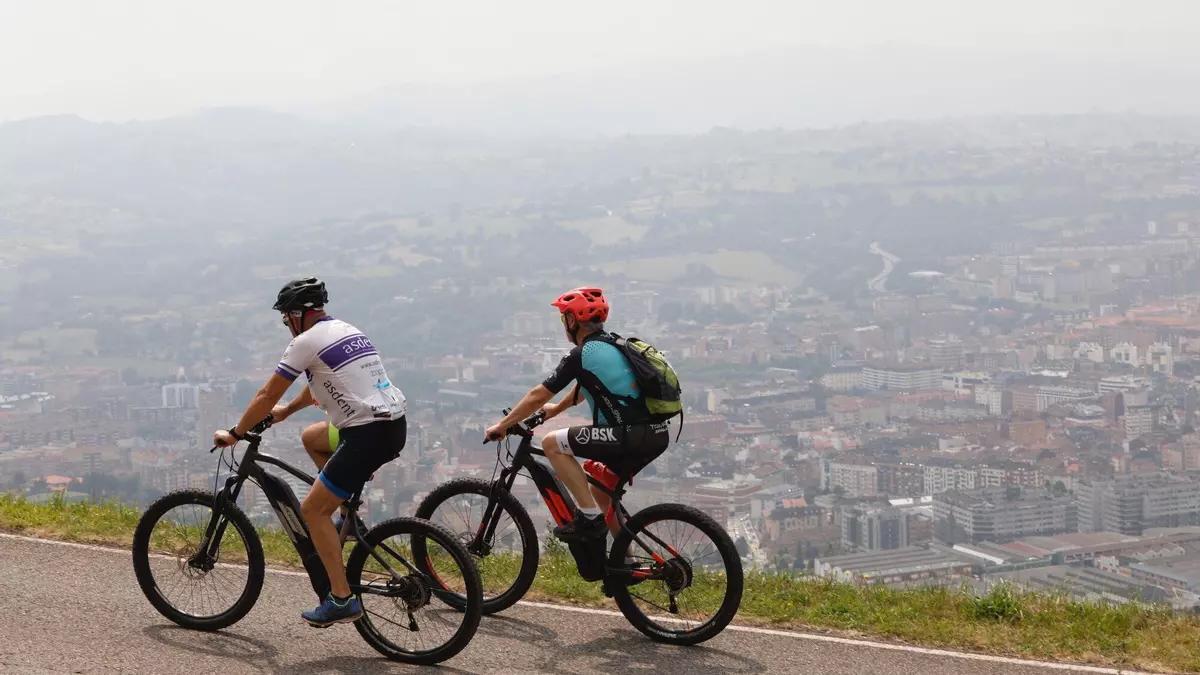 Dos ciclistas con la ciudad de Oviedo al fondo afectada por la contaminación.