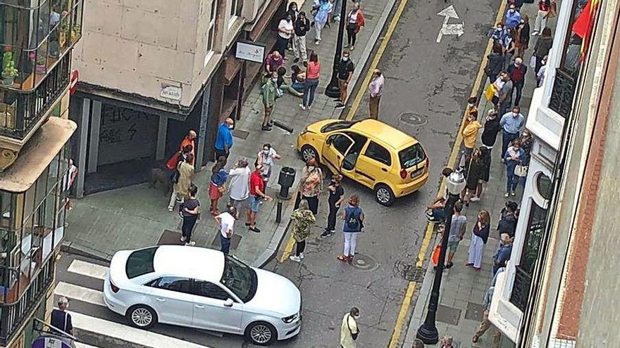 La mujer, tendida en el suelo, junto a los dos vehículos implicados en el choque ocurrido en la calle Cabrales, en Gijón.