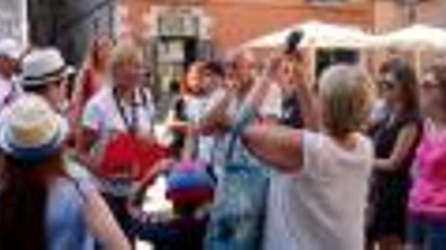 Un grup de turistes amb la seva guia, que porta penjat al coll un micròfon, i turistes caminant pel carrer de la Força de Girona.