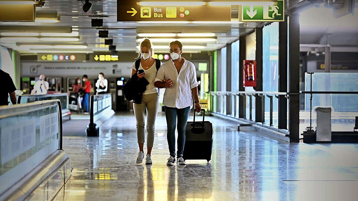 Una pareja de jóvenes
camina por los pasillos de
un aeropuerto con una
maleta.  FERNANDO VILLAR / EFE