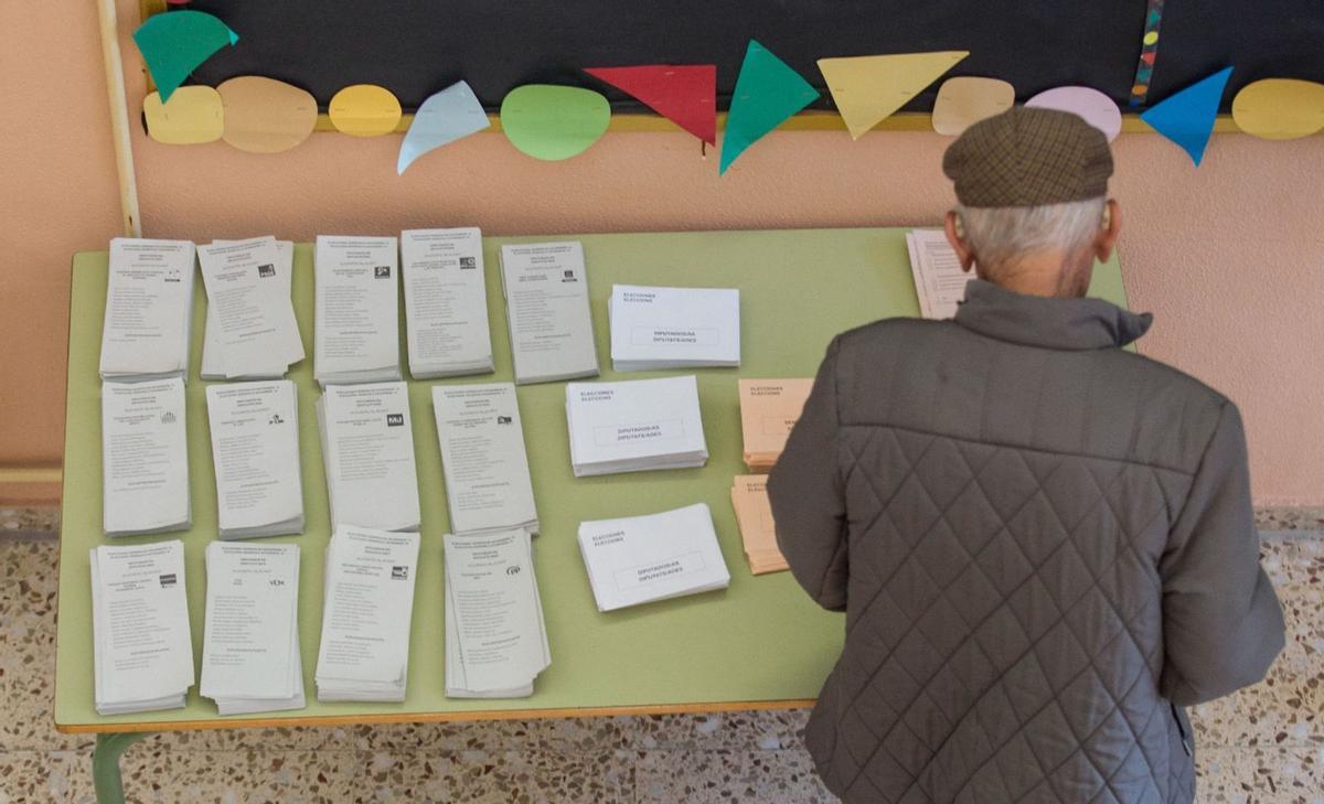 Un hombre, ante una mesa con papeletas de los distintos partidos en un colegio electoral en las elecciones de 2019. | ALEX DOMÍNGUEZ