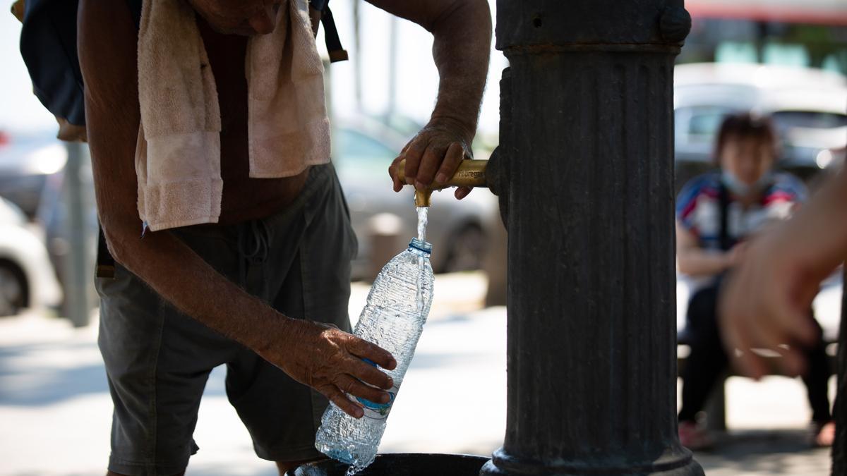 Un hombre llena una botella de agua en una fuente, en Barcelona.