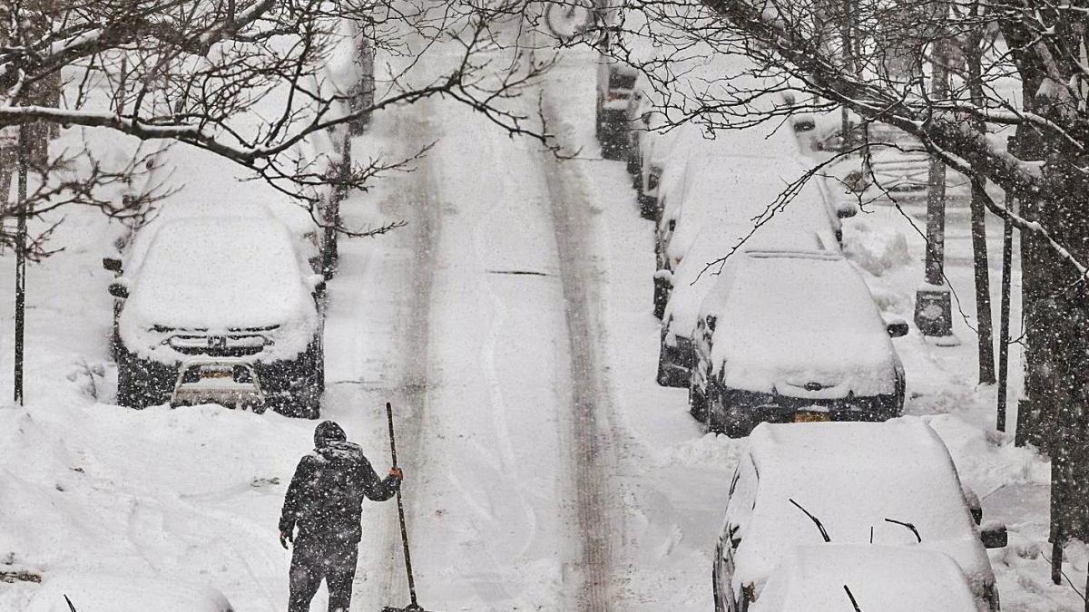 Un home treu neu en un carrer ple de cotxes enterrats a Nova York.
