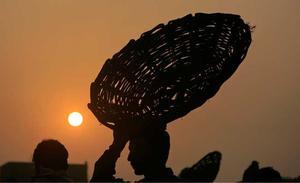 Un treballador porta una cistella mentre surt el sol, a Lahore (Pakistan).