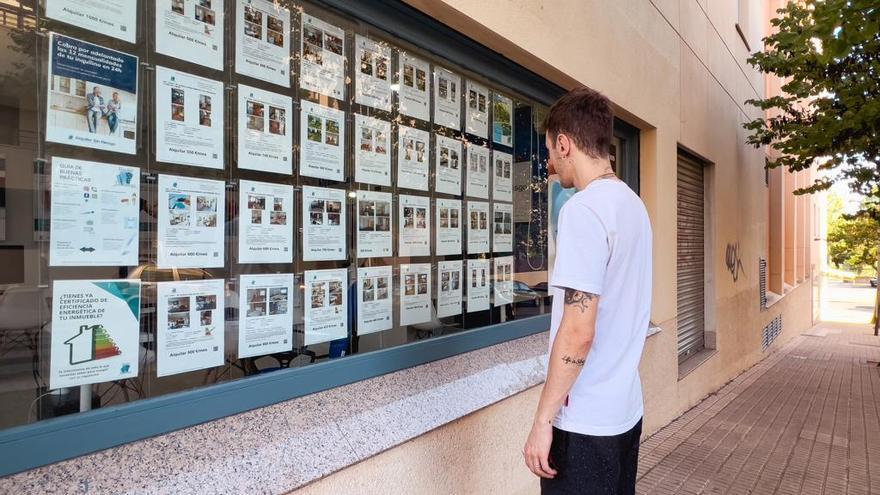 Un joven mira anuncios de venta de pisos en una agencia inmobiliaria.
