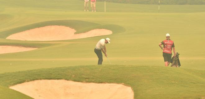 El golfista neozelandés Ryan Chisnall (C) golpea un tiro en la calle a través de la bruma espesa de los incendios forestales en el primer hoyo en el primer día del torneo de golf Open de Australia en Sydney.