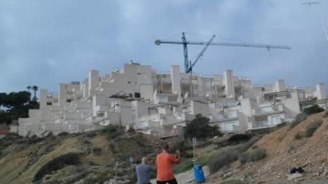 Dos hombres practican deporte sobre el arenal de Cala Lanuza, con los apartamentos inacabados al fondo.