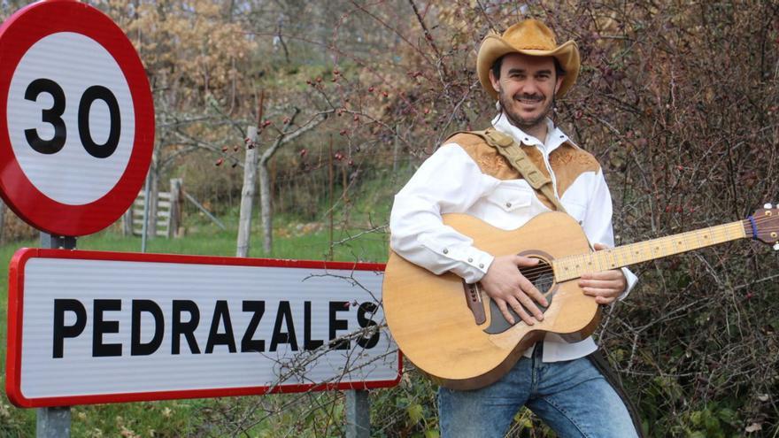 Jesús Enrique Cuadrado posa con su guitarra junto a una de las señales que indica el acceso a Pedrazales. | ARACELI SAAVEDRA