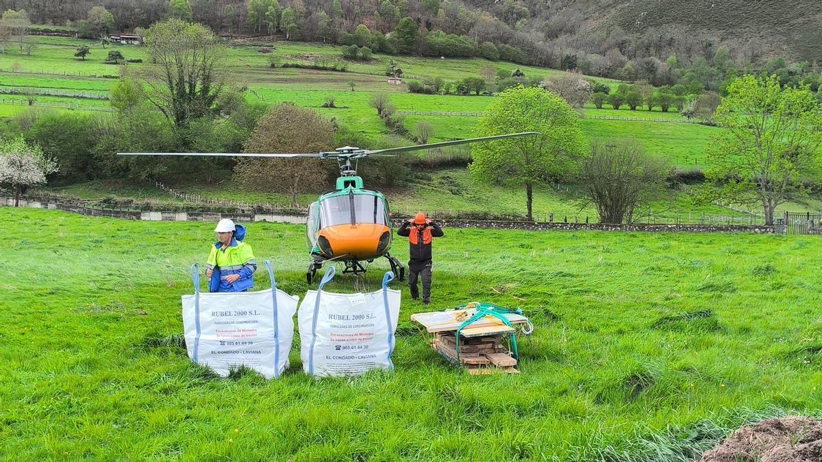 Dos operarios con material y el helicóptero al fondo.