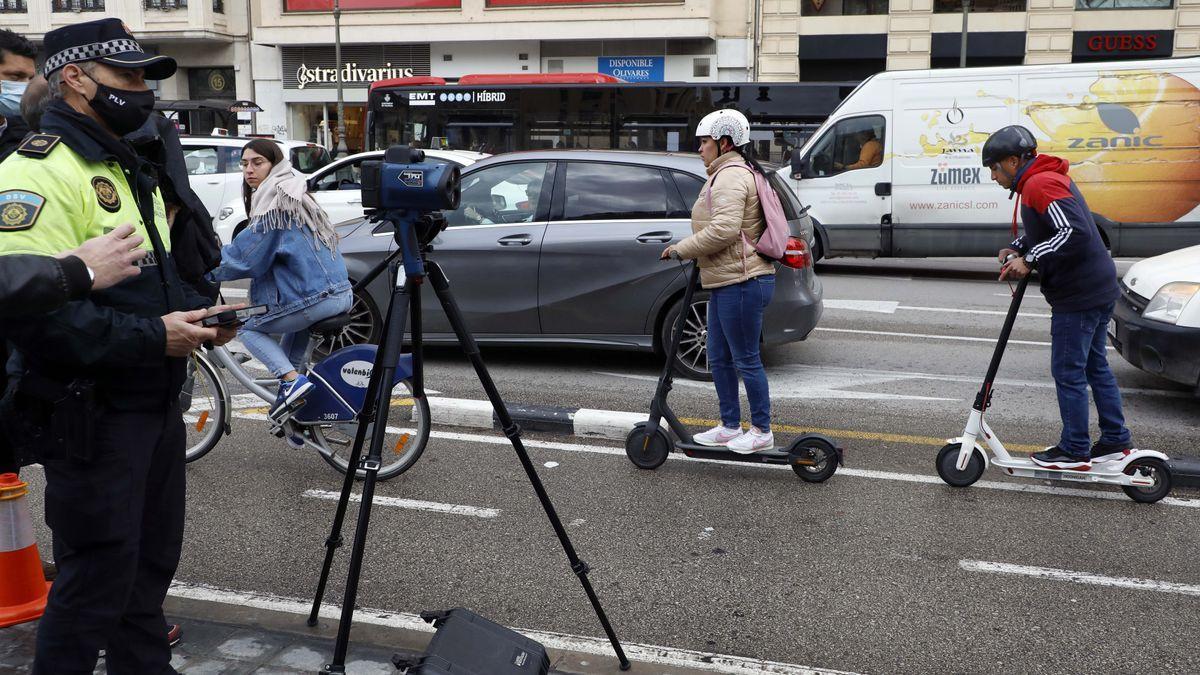 Un agente controla la velocidad con una tablet y el radar, mientras dos conductores circulan en patinete por la calle Xàtiva. / M.A. MONTESINOS