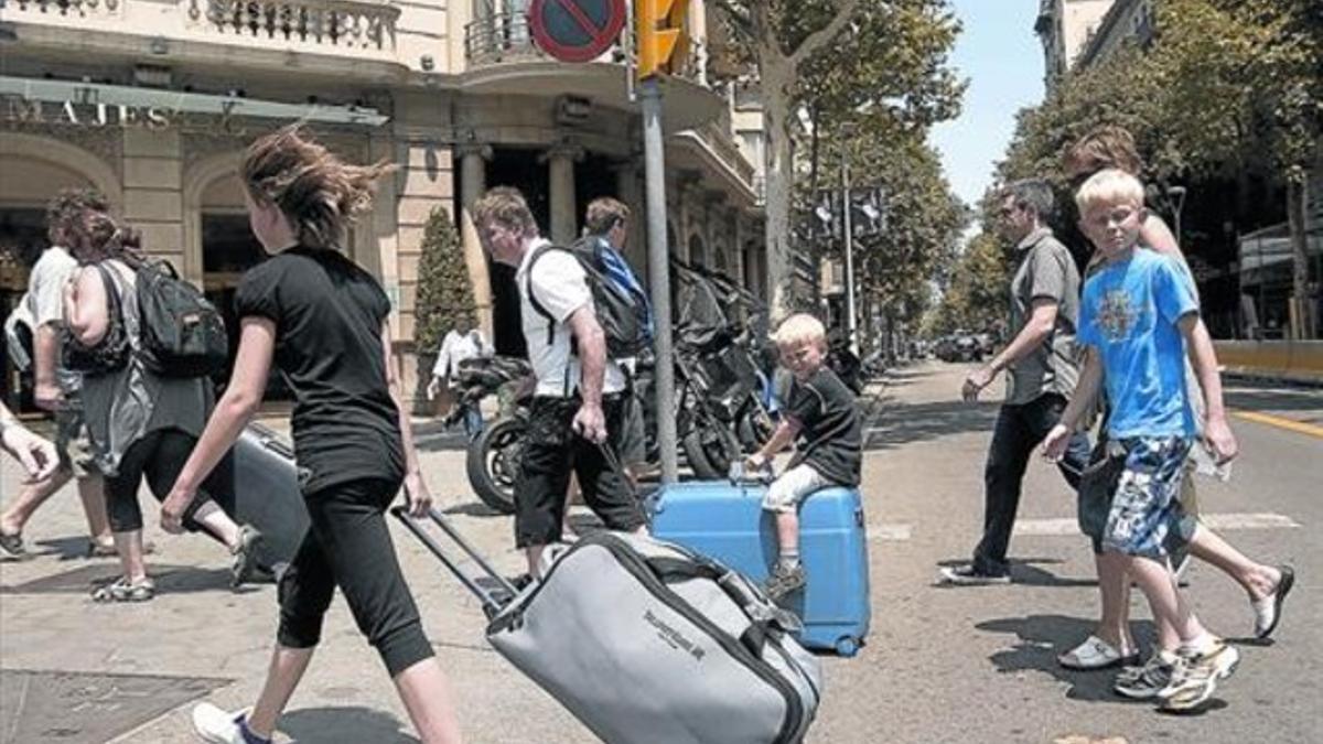 Turistas con maletas rumbo  a su alojamiento recorren el paseo de Gràcia.