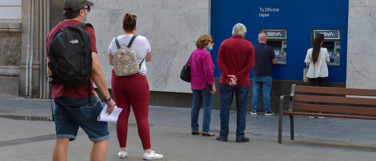 Varias personas hacen cola ante los cajeros automáticos de una entidad bancaria.