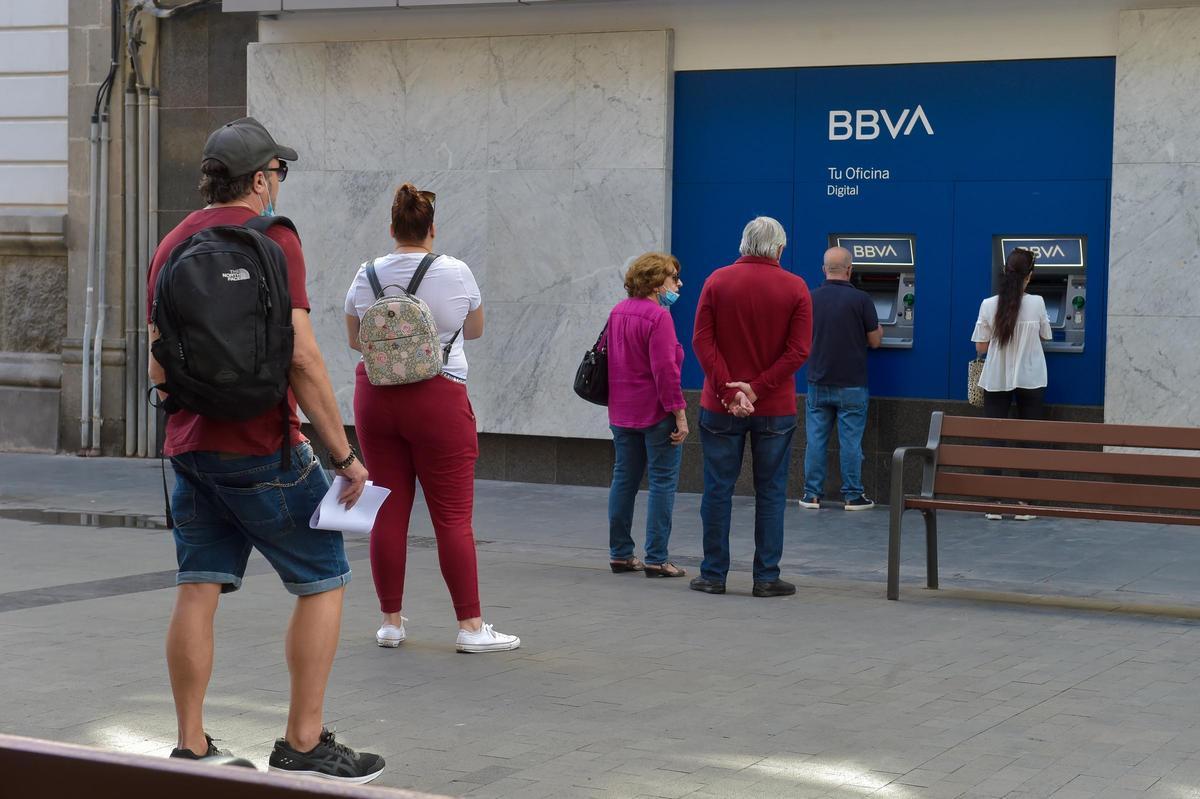Varias personas hacen cola ante los cajeros automáticos de una entidad bancaria.