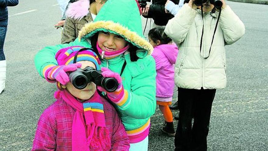 Arriba una de las niñas enseña a su compañera a mirar por los prismáticos; a la izquierda, otro pequeño aprende, en el aula, a manejar los binoculares. / t. c.