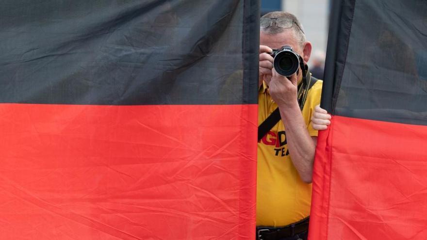 Archivfoto von einer Pegida-Demontration in Leipzig vom Juni 2020. Ein Teilnehmer einer Kundgebung der islam- und ausländerfeindlichen Pegida-Bewegung fotografiert auf dem Altmarkt zwischen zwei Deutschlandfahnen die Teilnehmer einer Gegendemonstration.