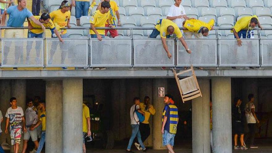 Un aficionado amarillo arroja una silla de madera a otro seguidor de la UD, ante la mirada de dos miembros de la seguridad privada de la entidad isleña.