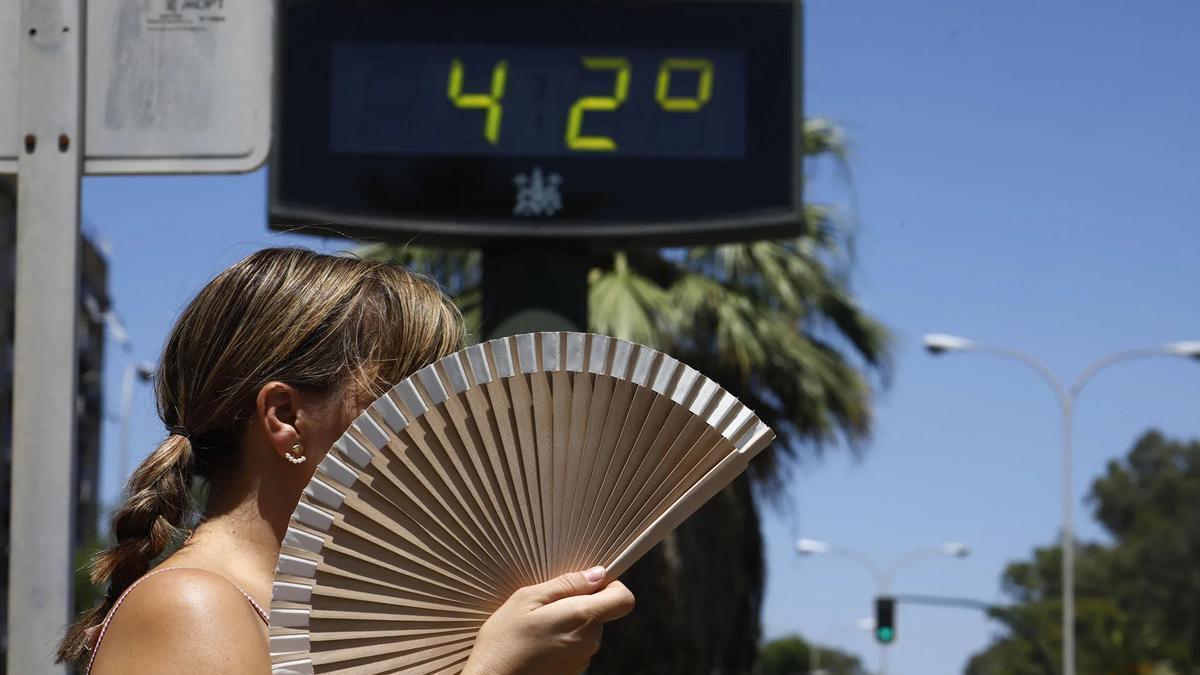 Una mujer se abanica mientras pasa por un termómetro de calle que marca 42 grados