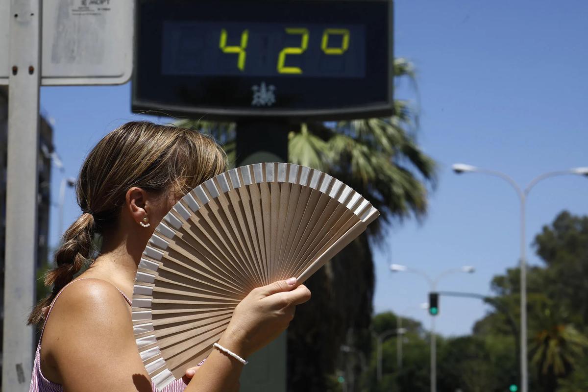 Una mujer se abanica mientras pasa por un termómetro de calle que marca 42 grados en Córdoba.