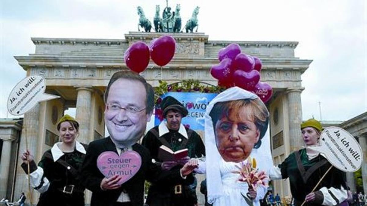 Dos activistas llevan máscaras de Hollande y Merkel, simulando una boda, en la puerta de Brandeburgo de Berlín, ayer.