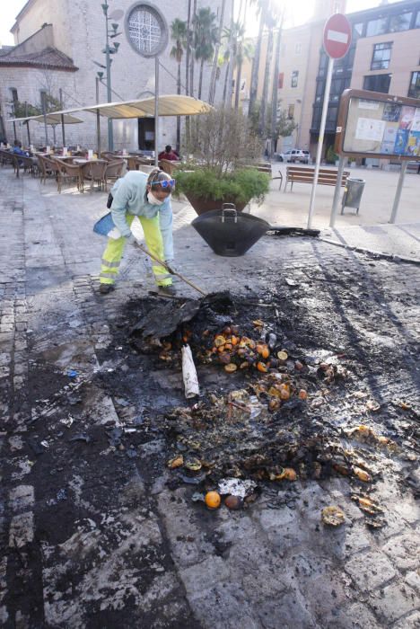 Carrers amb restes de mobiliari urbà cremat, contenidors per terra i treballadors de la brigada treballant