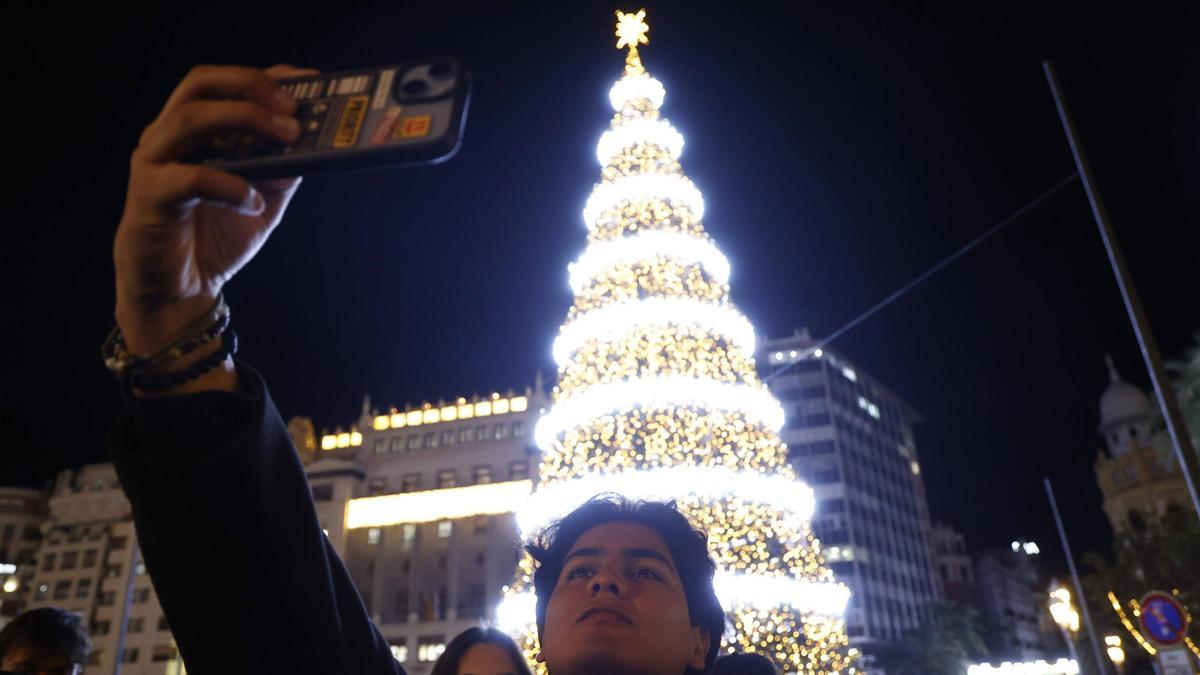 Un joven hace un selfi ante el árbol de Navidad de la plaza del Ayuntamiento de València.