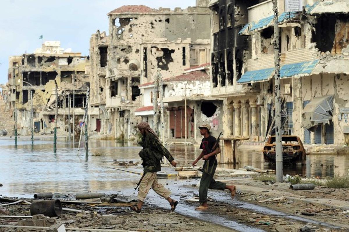 Uns milicians travessen un dels carrers de Sirte, ciutat natal de Muammar al-Gaddafi, completament destrossada durant la batalla.