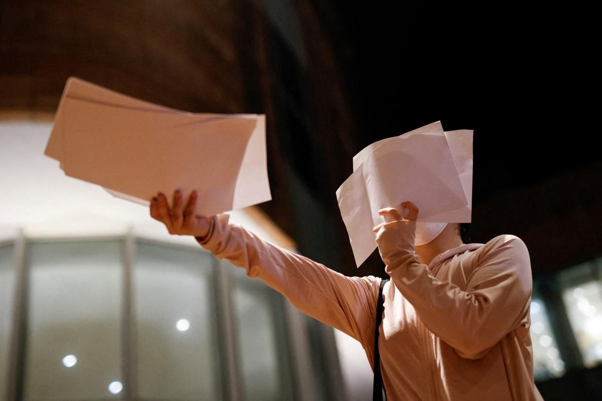 Una mujer reparte folios blancos durante una concentración en la universidad de Hong Kong para recordar a las víctimas del incendio en Urumqi.