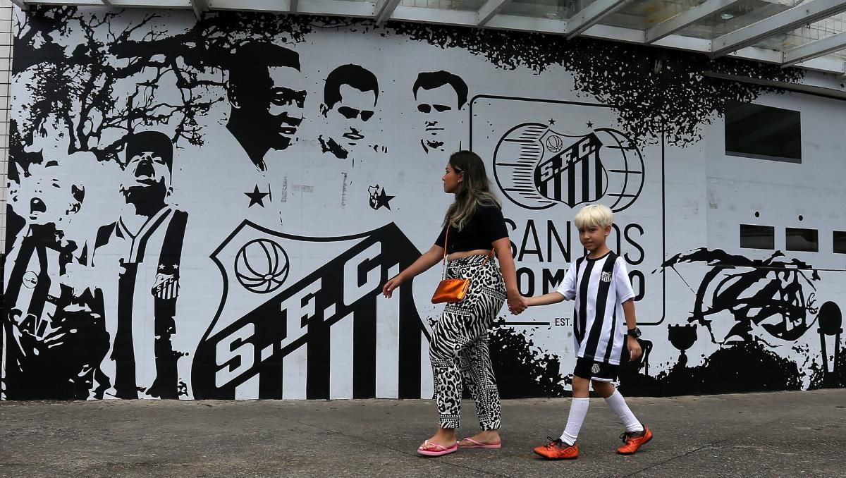 Una mujer y un niño caminan frente a un mural del Club Santos en el estadio Urbano Caldeira en la Vila Belmiro, tras conocerse la noticia de la muerte de la leyenda del fútbol brasileño Pelé, hoy, en la ciudad de Santos (Brasil).