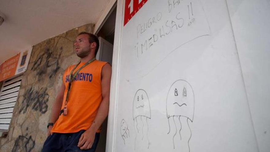 Daniel Río, junto a un cartel que alerta de la presencia de medusas en la playa, en el puesto de salvamento de Luanco.