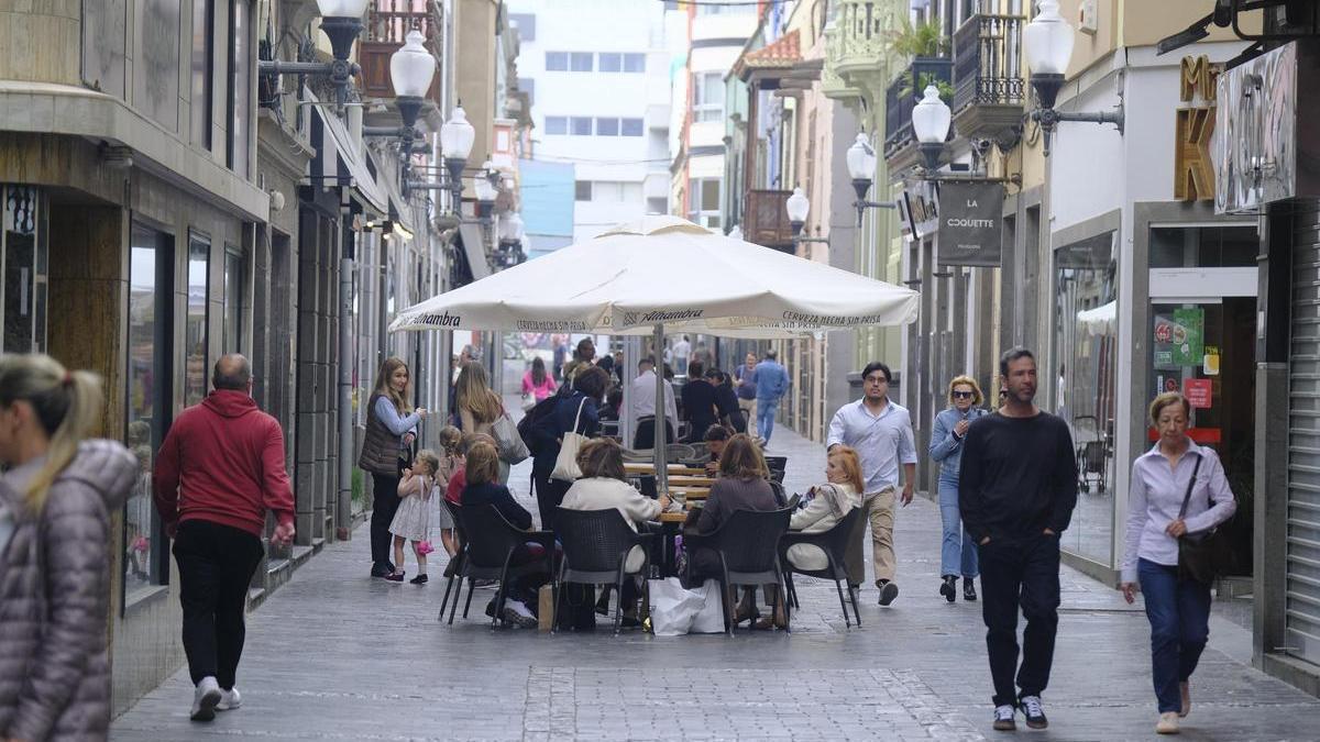 Varias personas pasean y consumen en una terraza en una calle de Canarias.