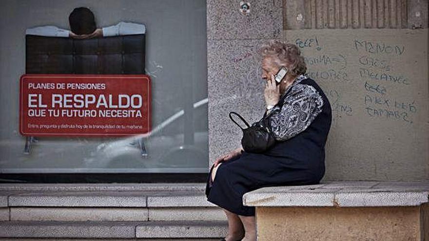 Una dona gran parla per telèfon al costat d&#039;un banc amb publicitat de plans de pensions.