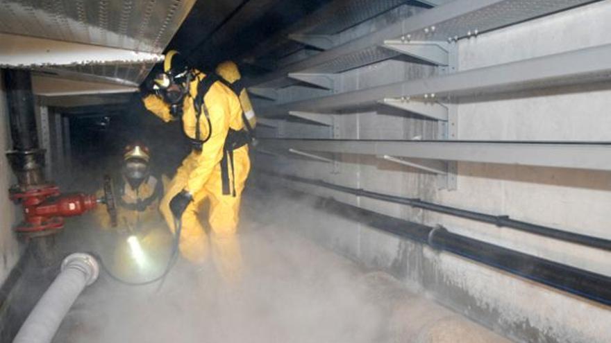 Dos bomberos del SEIS taponan una tubería en la galería subterránea para frenar la fuga de gas simulada. | j.c. castro