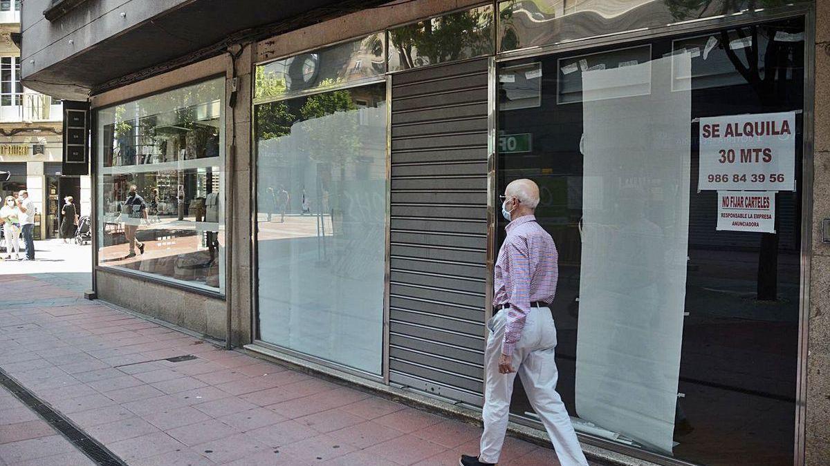 Un hombre con mascarilla pasa junto a un local comercial cerrado.