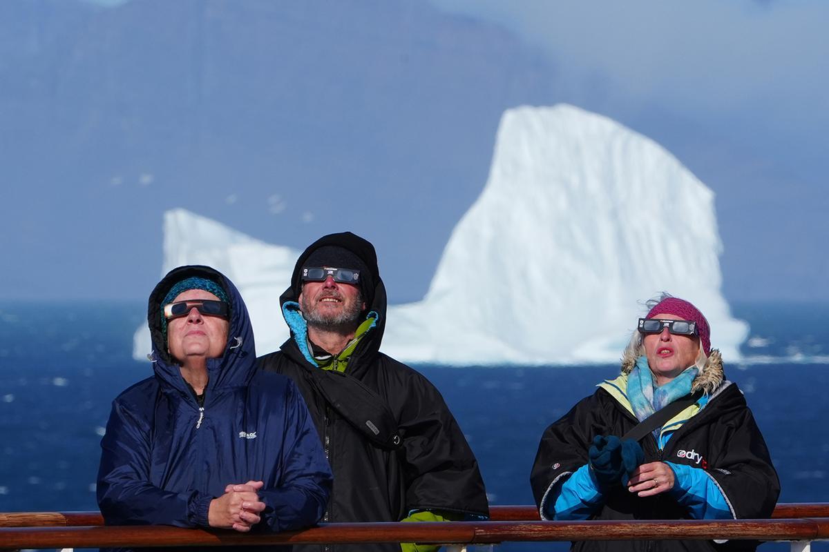 Pasajeros a bordo del barco Ambition, de la naviera Ambassador, usan gafas protectoras para ver el eclipse de Sol mientras navegan por la costa de Groenlandia.