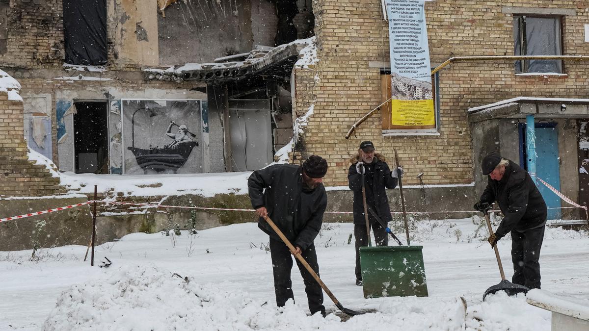 Residentes de la población ucraniana de Horenka quitan nieve junto a un edificio destruido, en el que se aprecia un grafiti de Banksy